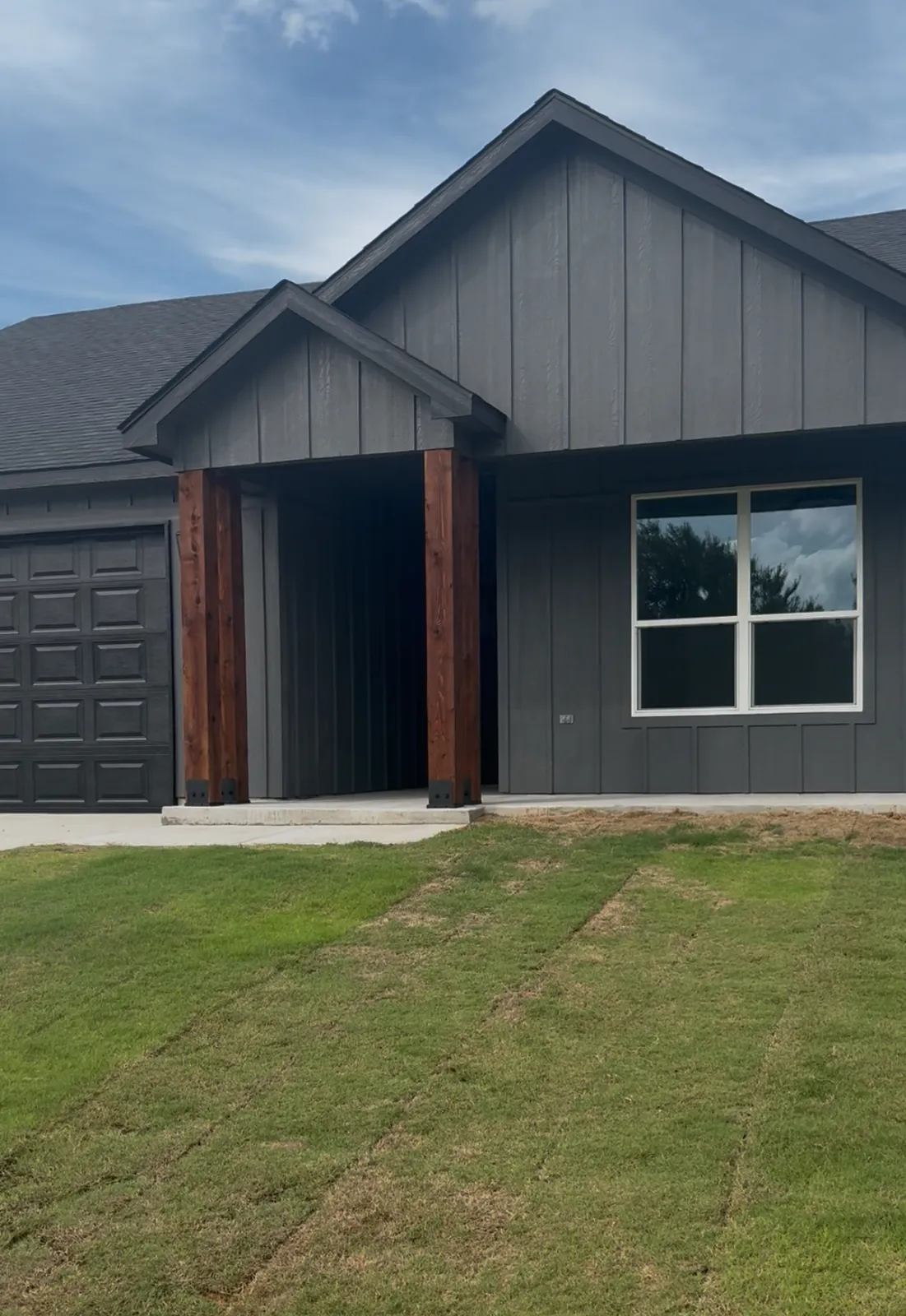 Newly built charcoal board-and-batten home with cedar porch posts