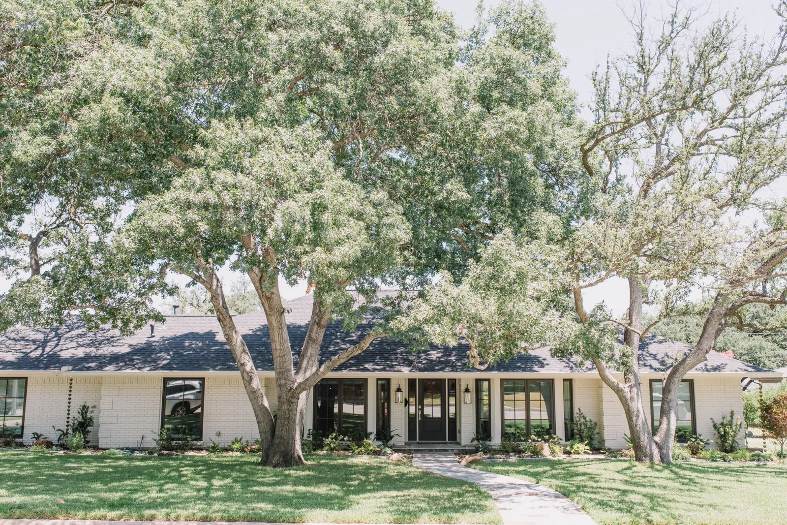 White brick ranch home under mature oaks